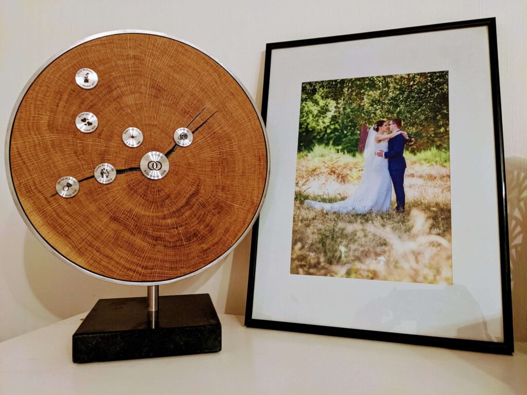 MyLivingTree Standobjekt Rustikal neben einem gerahmten Hochzeitsfoto — handgefertigte Baumscheibe aus Eiche mit gravierten Meilensteinen als Hochzeitsgeschenk